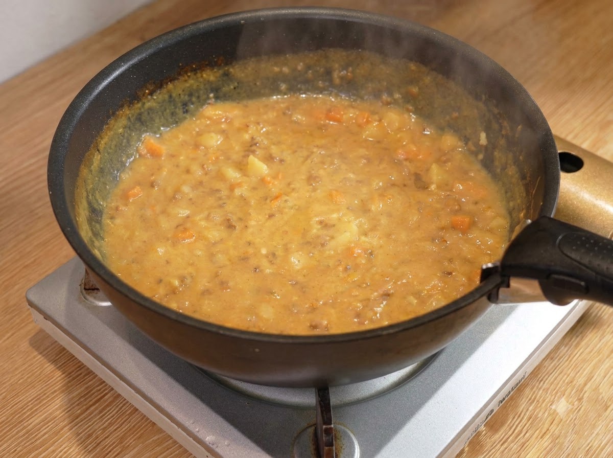 Drewniana łyżka mieszająca gęsty, bulgoczący sos mięsny curry na czarnej patelni na palniku.