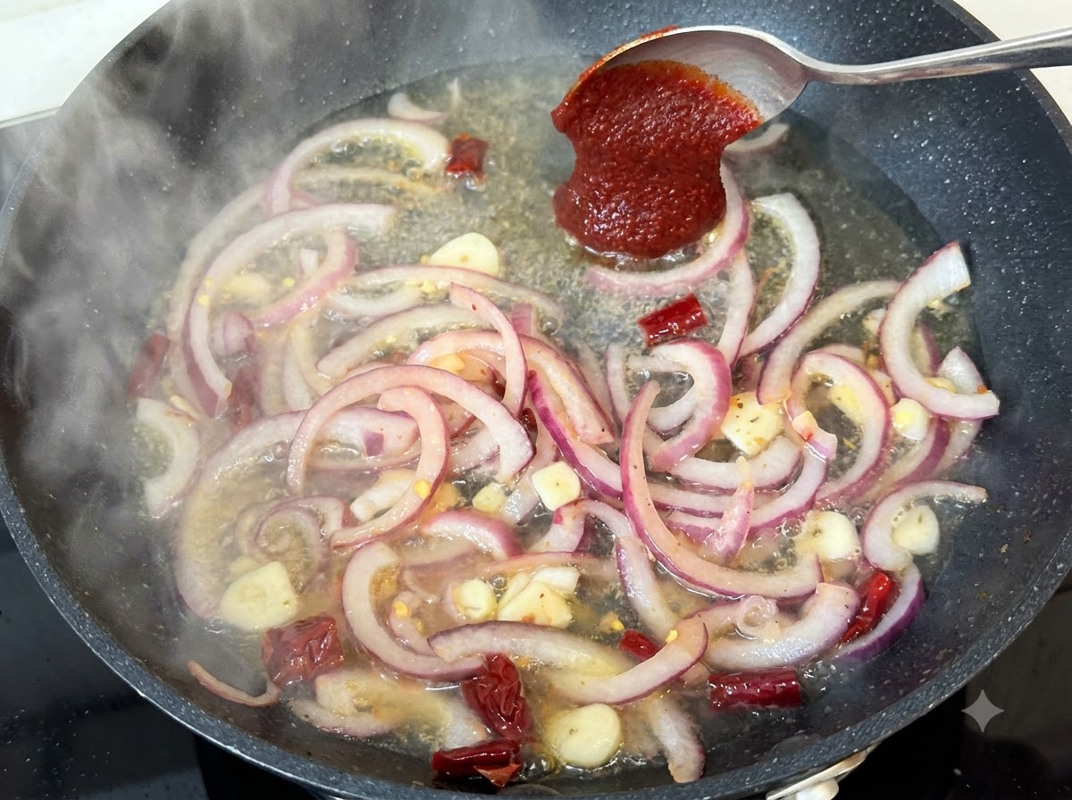 Łyżka koreańskiej pasty chili dodawana do płynu na patelni z cebulą i przyprawami.