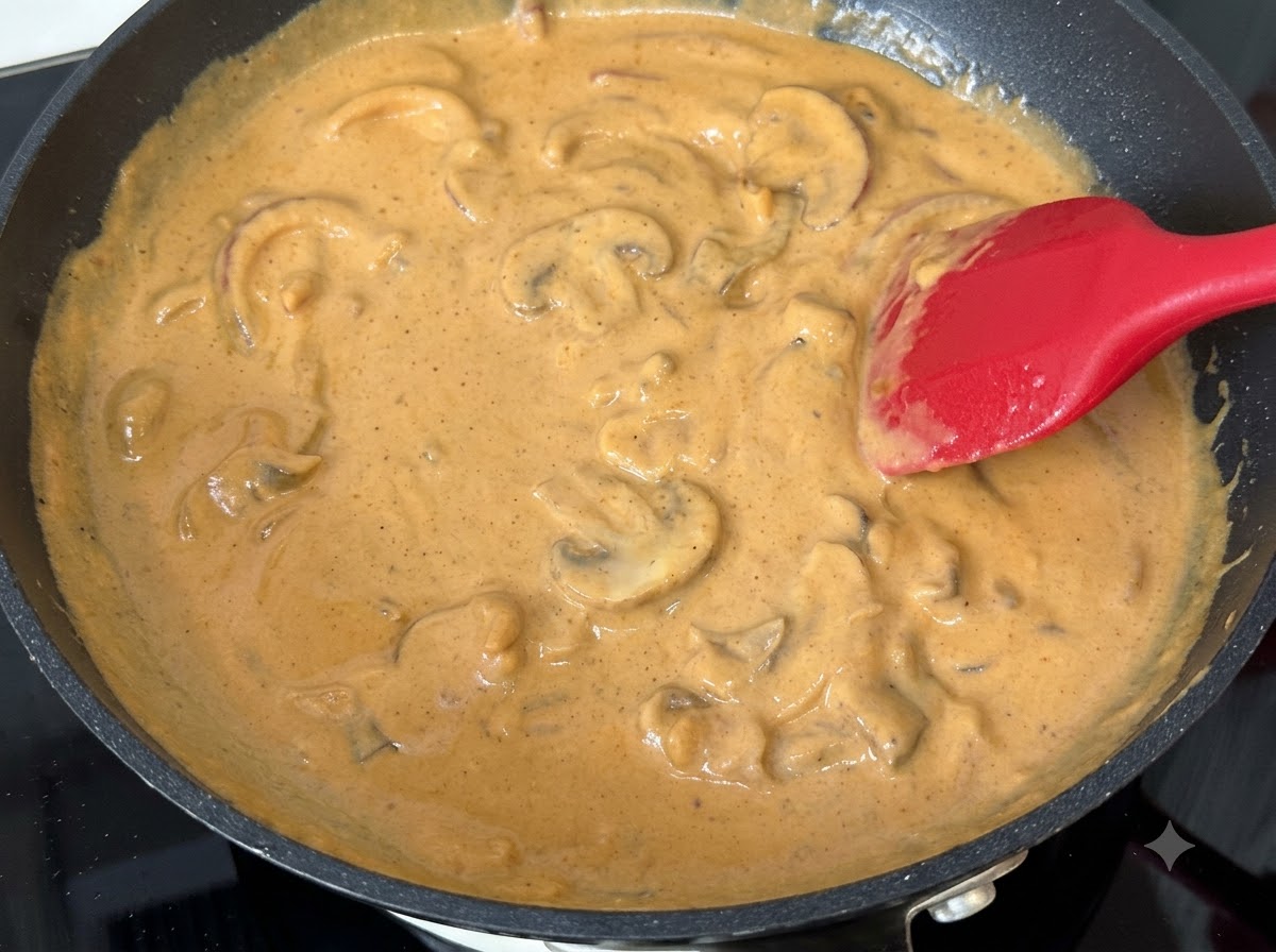 Plastry grzybów wymieszane w duszącym się kremowym sosie curry na patelni.