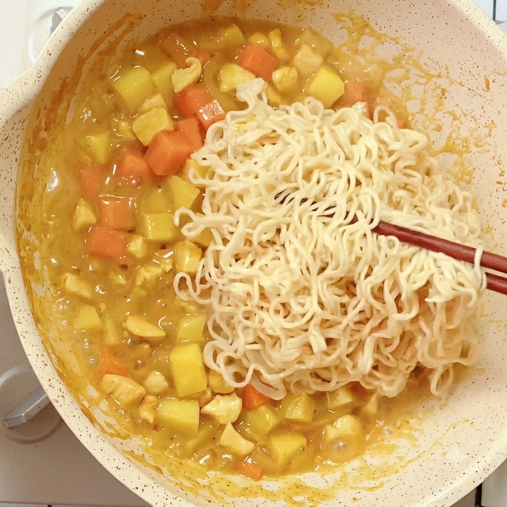 Wstępnie ugotowany makaron błyskawiczny umieszczany pałeczkami na patelni z redukującą się mieszaniną curry.