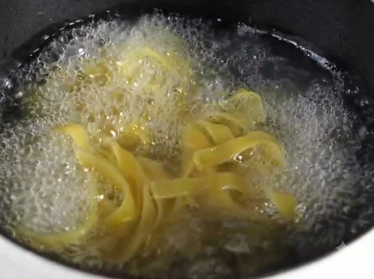 Zbliżenie ugotowanego makaronu fettuccine ułożonego schludnie na okrągłym szarym talerzu.