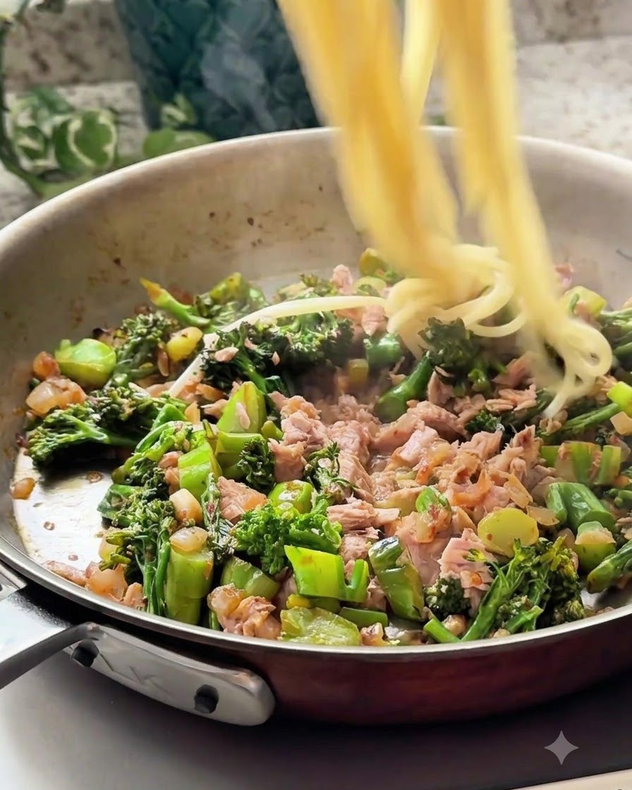 Ugotowane nitki spaghetti wrzucane na patelnię z mieszanką tuńczyka i warzyw.