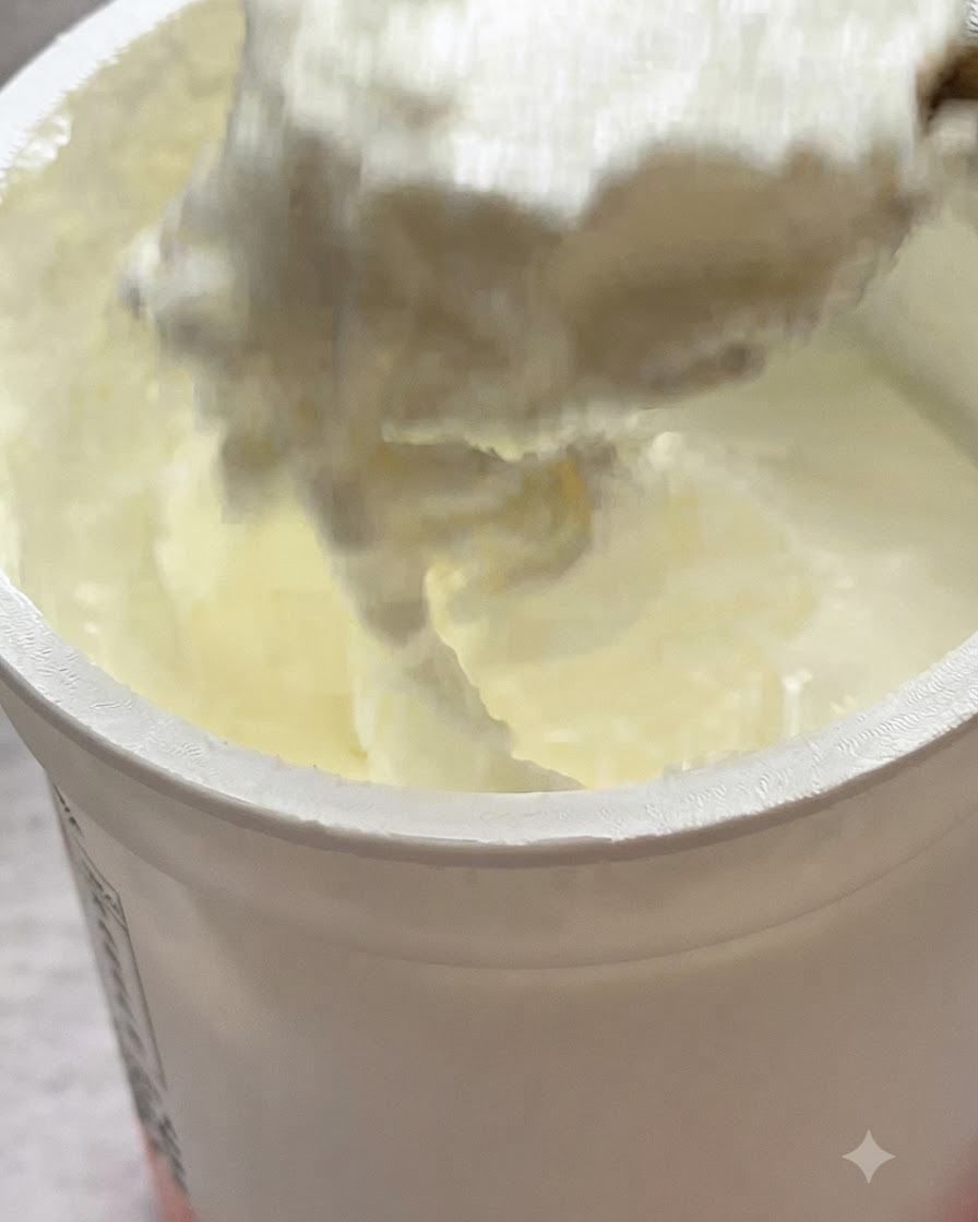 Łyżka jogurtu naturalnego nakładana na wierzch makaronu na patelni.