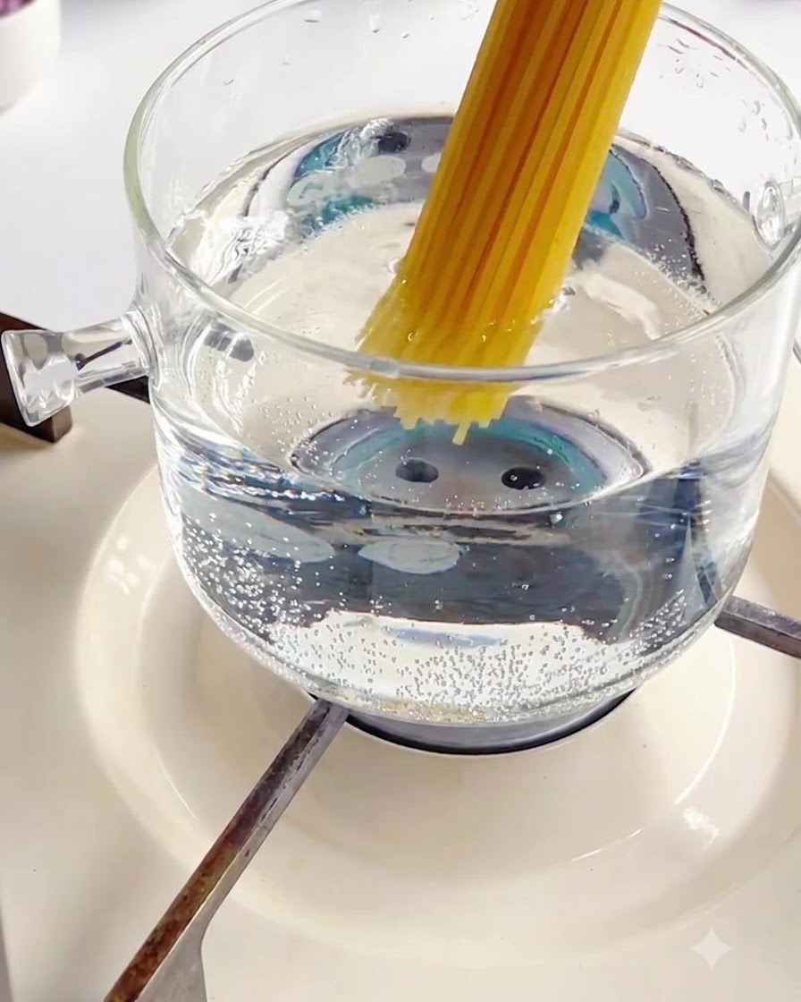 Wkładanie wiązki suchego makaronu spaghetti do bulgoczącego szklanego garnka z gorącą wodą.