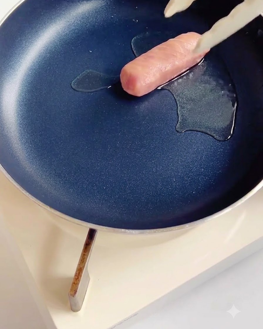 Nacięta kiełbasa smażąca się na ciemnej patelni nieprzywierającej z niewielką ilością oleju.
