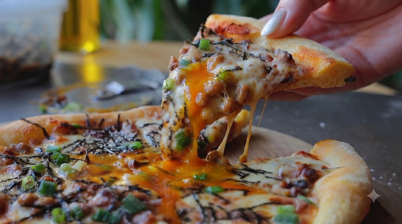 Świeżo upieczony kawałek pizzy z natto podnoszony z ciągnącymi się nitkami sera i spływającym żółtkiem.