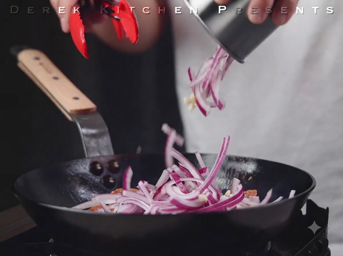 Pokrojona czerwona cebula i czosnek wrzucane na patelnię na salami.
