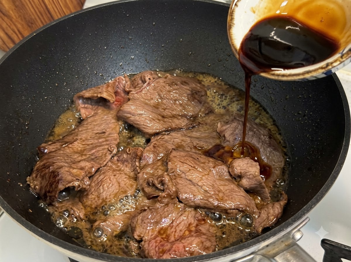 Sos teriyaki wlewany na patelnię z pokrojoną tłustą wołowiną do duszenia i redukcji.