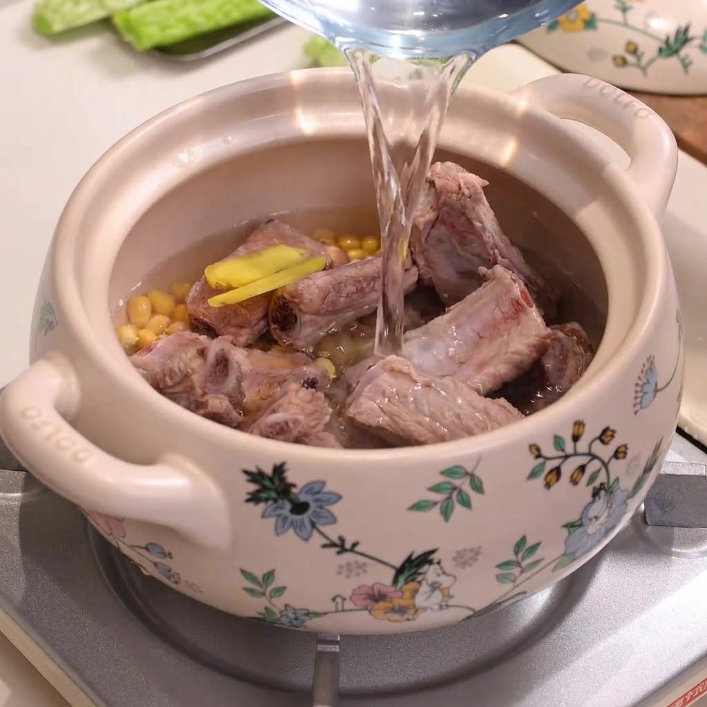 Woda wlewana z dzbanka do ozdobnego ceramicznego garnka wypełnionego żeberkami i soją.
