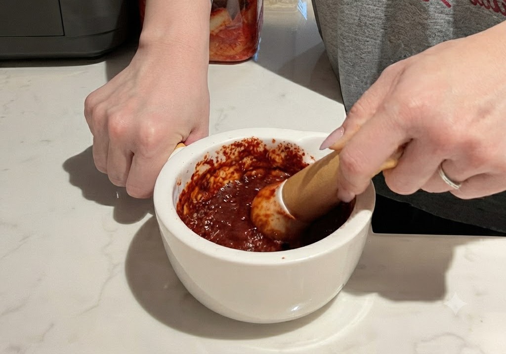 Ucieranie pasty z czerwonego chili i czosnku w białym ceramicznym moździerzu przy użyciu drewnianego tłuczka.