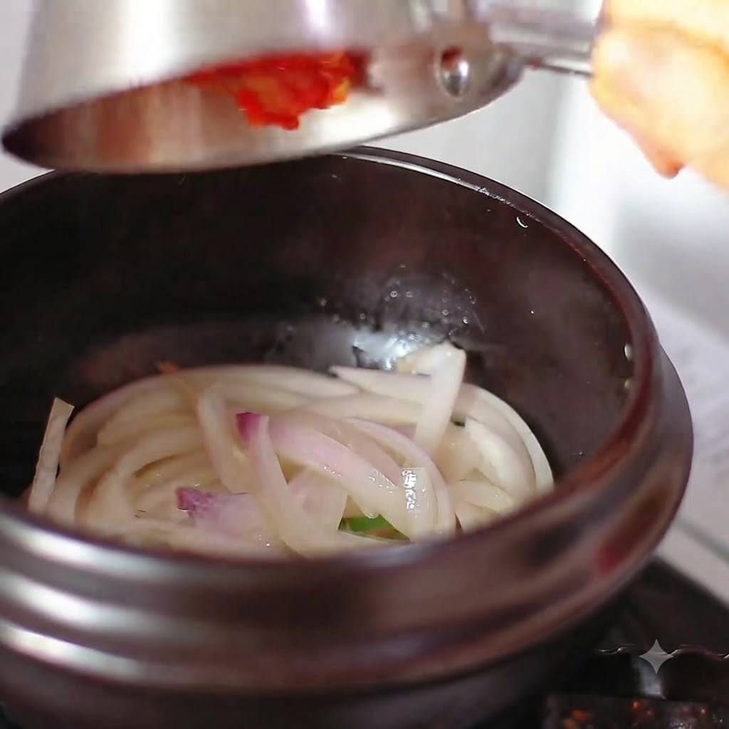 Kimchi i ostra papryka wsypywane do naczynia z podsmażoną cebulą.