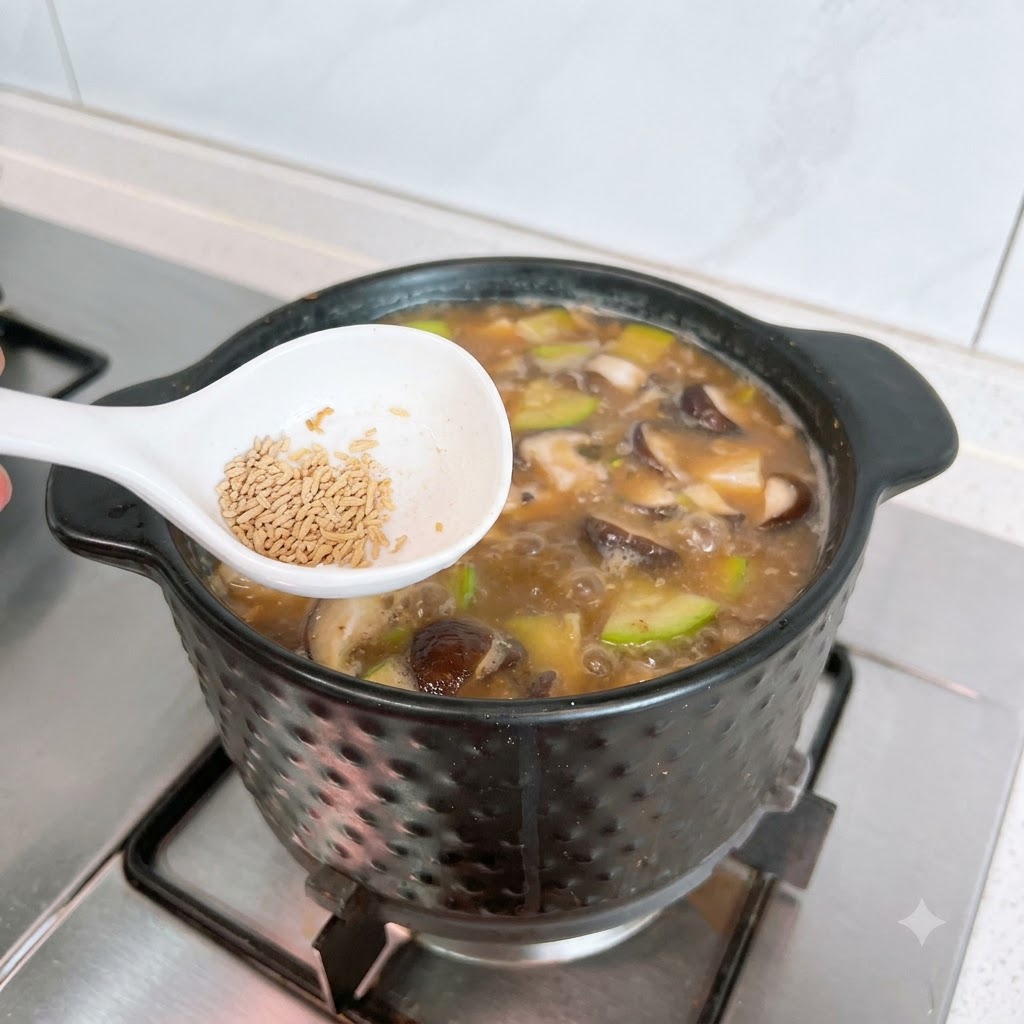 Biała łyżka z wołowym bulionem w proszku umieszczona tuż nad bulgoczącym garnkiem z Doenjang Jjigae.