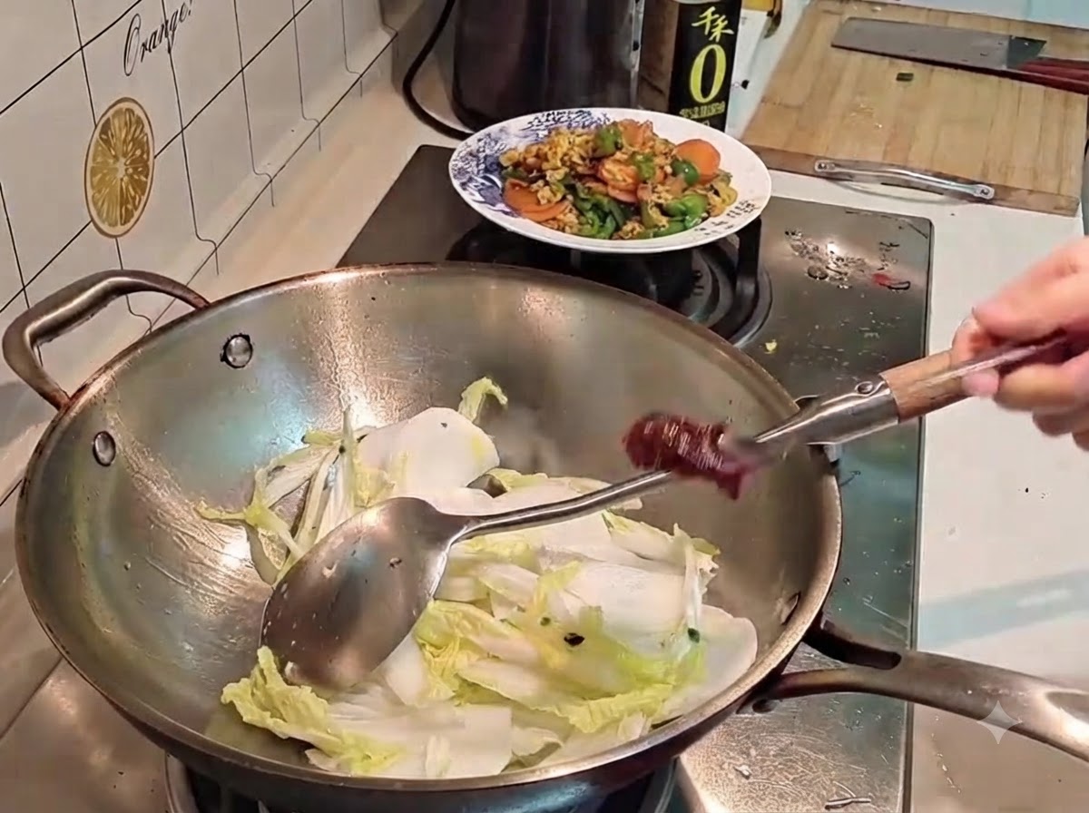 Dłoń trzymająca metalową łyżkę pełną ciemnoczerwonej koreańskiej pasty chili nad wokiem wypełnionym kapustą i rzodkwią.