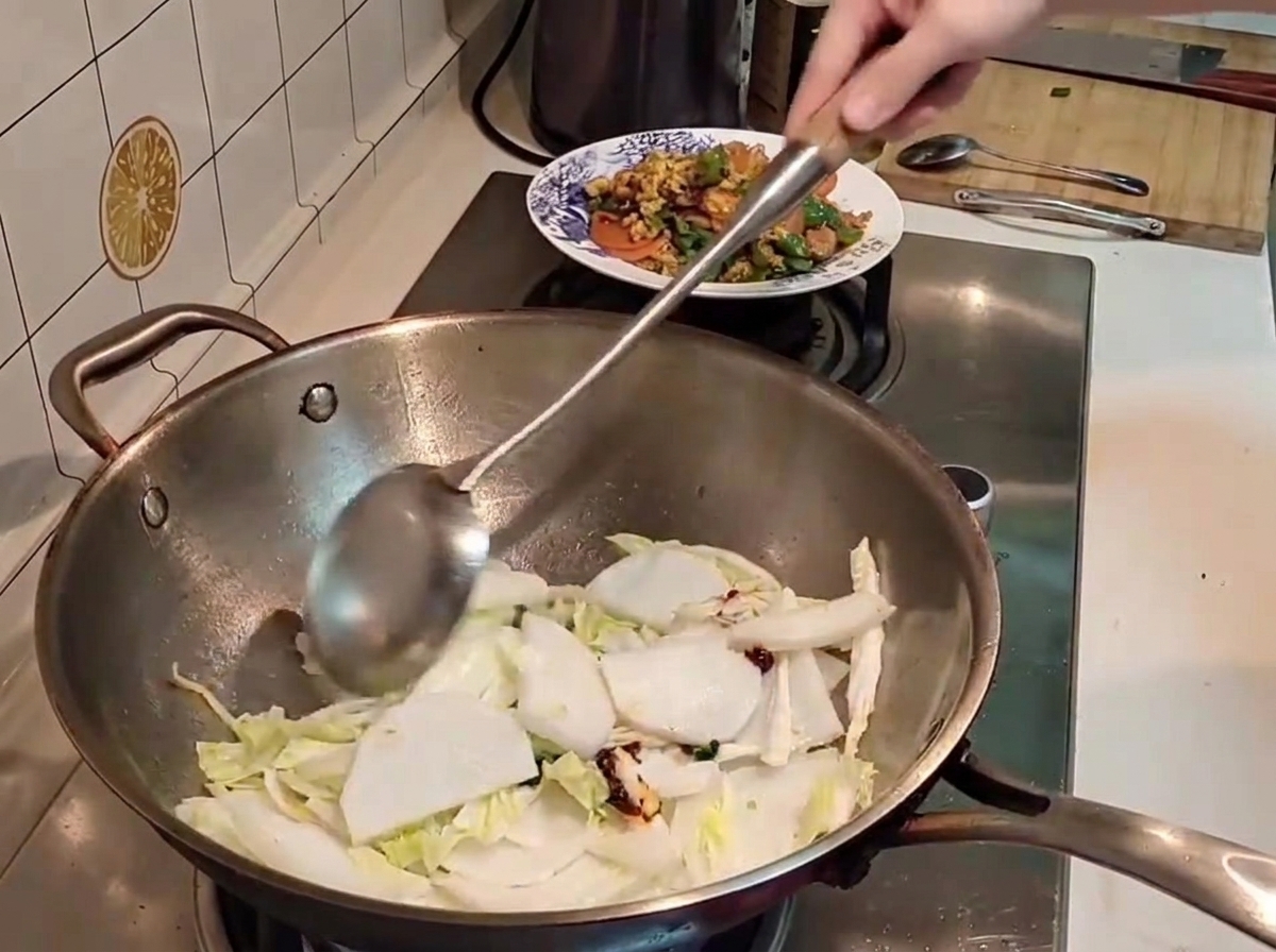Metalowa szpatułka mieszająca kawałki kapusty pekińskiej i białej rzodkwi z czerwoną pastą chili w gorącym woku.