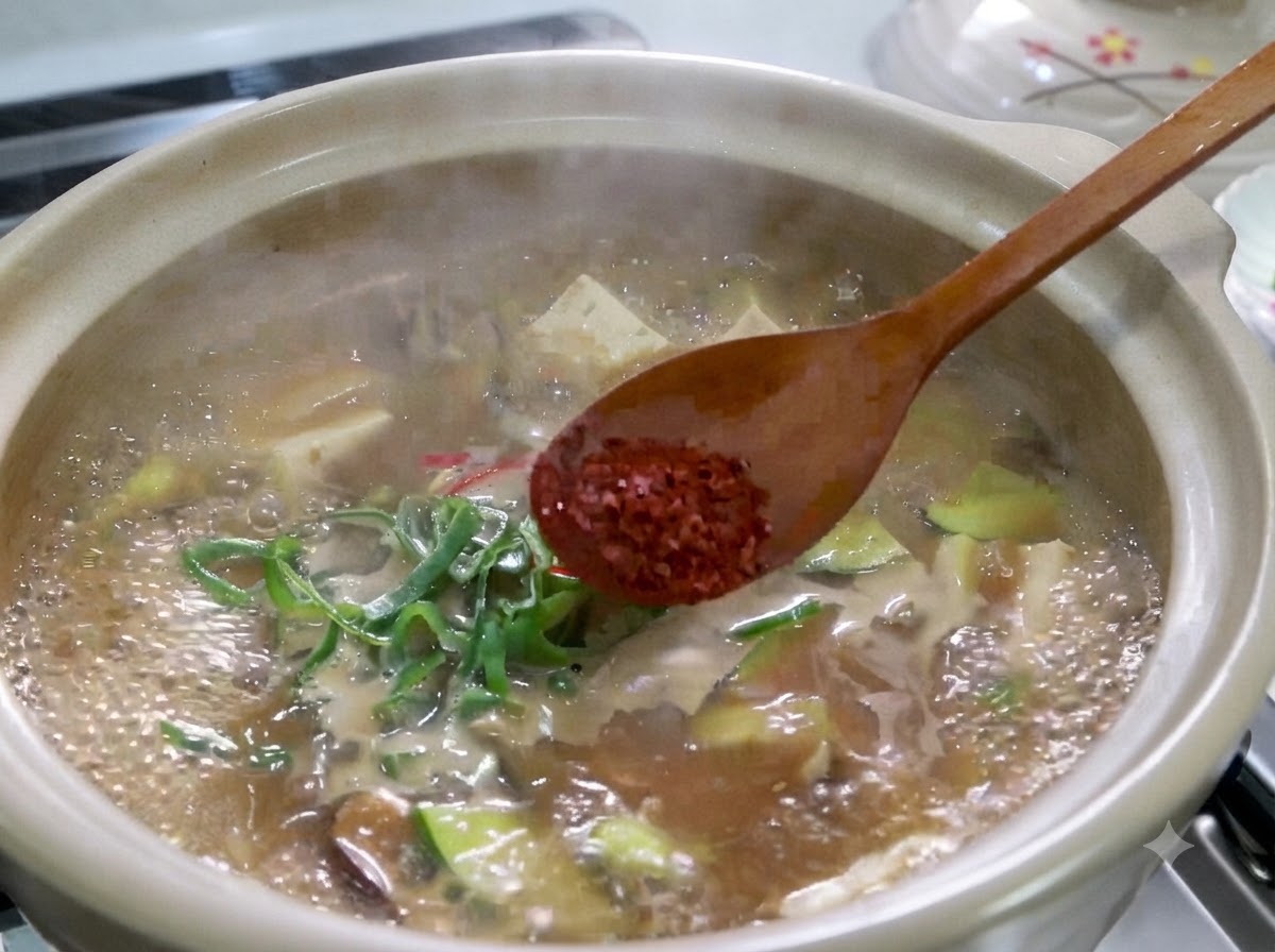 Drewniana łyżka trzymająca czerwone chili w proszku nad gotującym się garnkiem koreańskiego gulaszu z pasty sojowej.