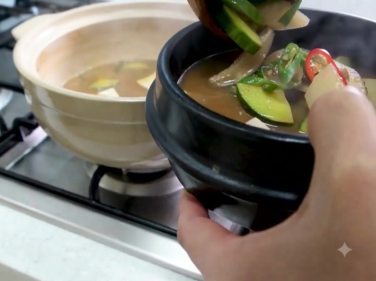 Chochla przekładająca gorące Doenjang Jjigae z cukinią i warzywami do czarnej kamiennej miski do serwowania.