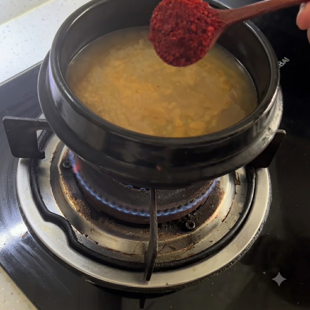 Drewniana łyżka trzymająca czerwony proszek chili nad garnkiem z doprawionym bulionem.