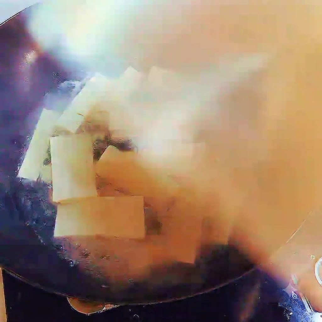Wok pełen gotującej się zupy i pasków tofu, starannie przykryty pokrywką.