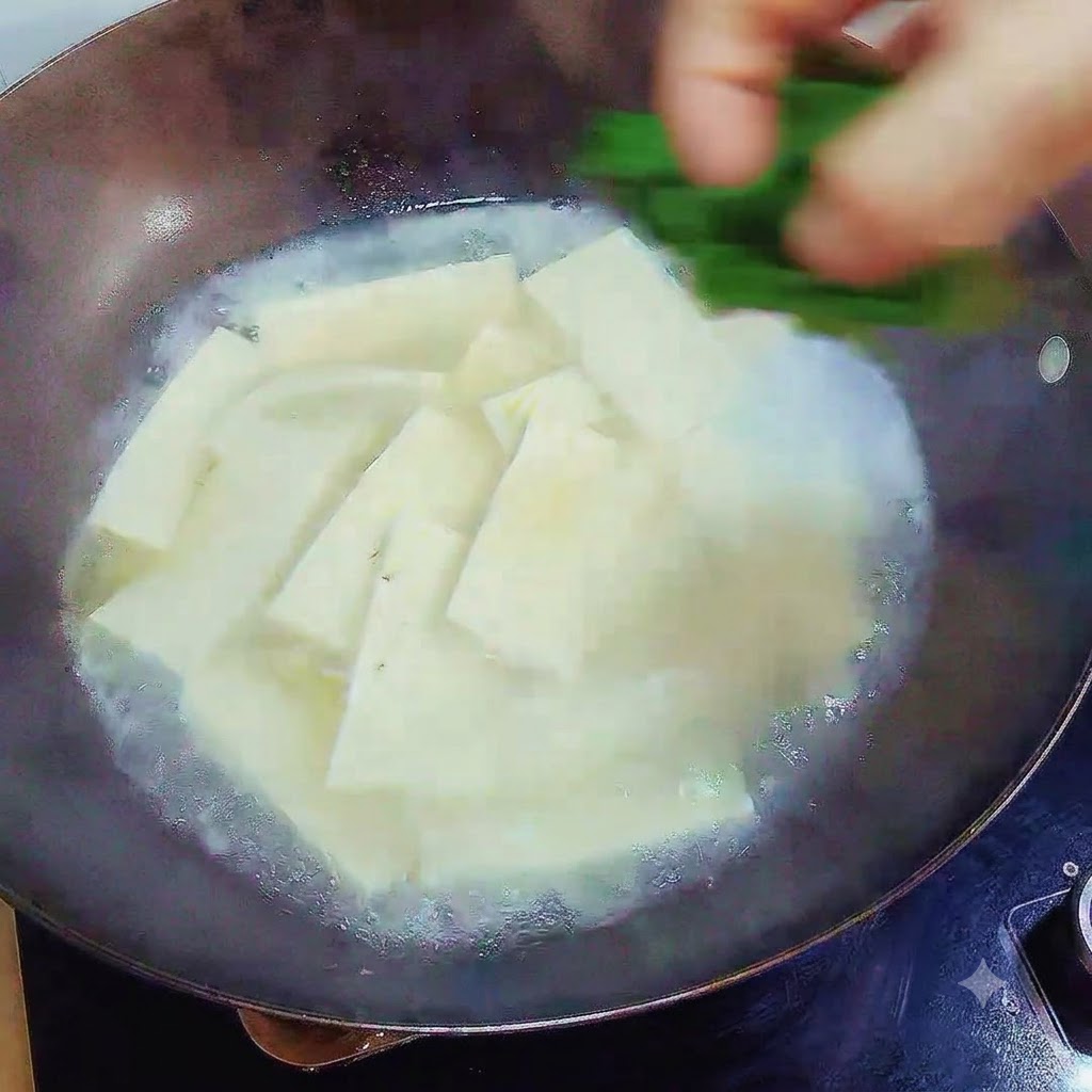 Dłoń sypiąca posiekany zielony szczypior na gotową zupę z tofu w woku.