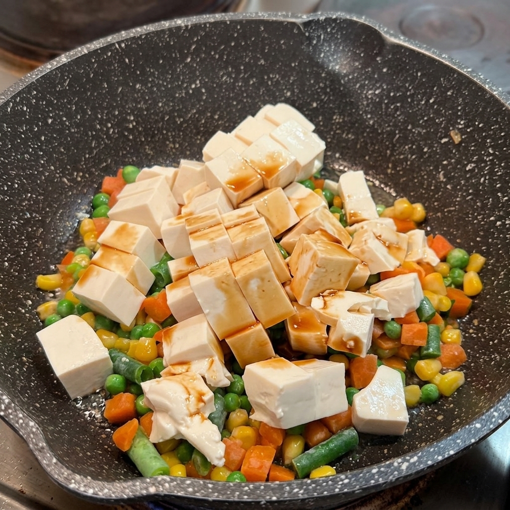 Sos sojowy rozprowadzony po kostkach miękkiego tofu i mieszance warzywnej na patelni.