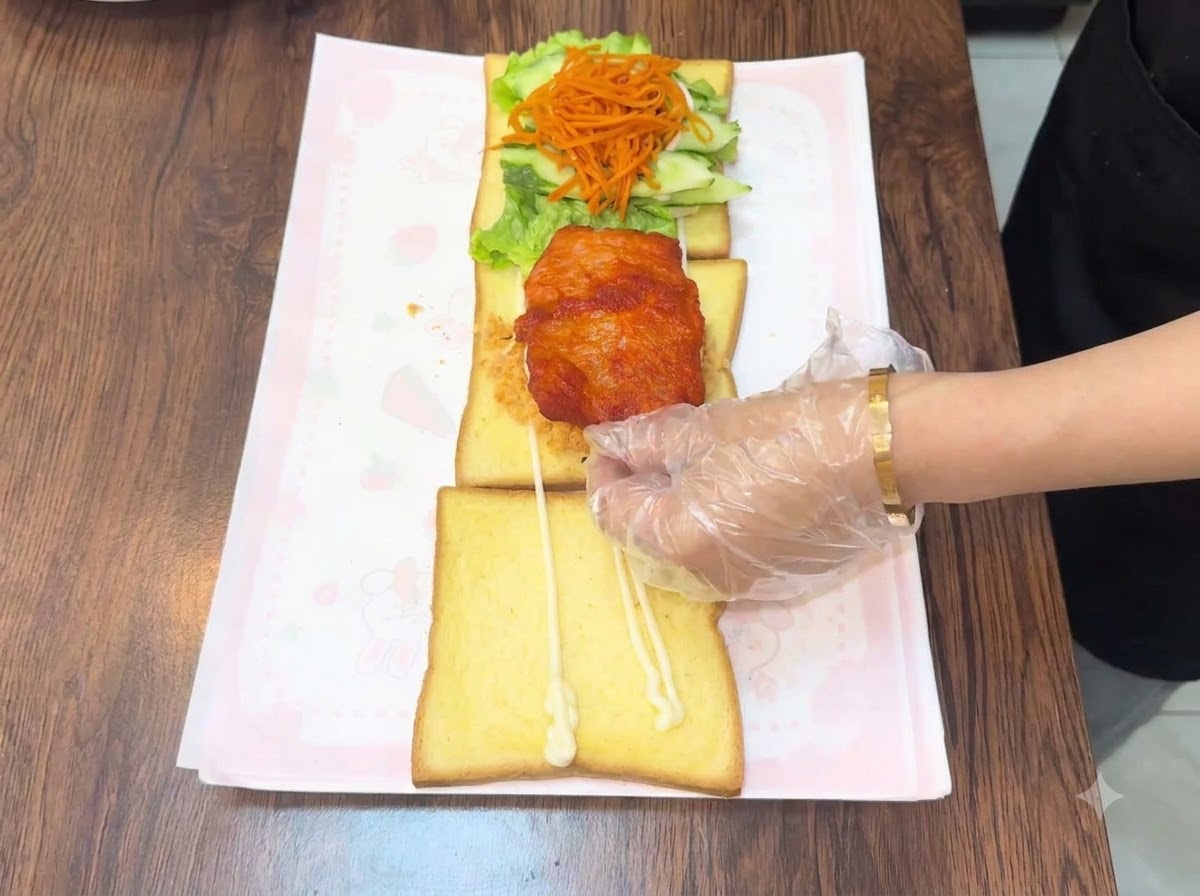 Ręka w rękawiczce umieszczająca ciepły smażony kotlet z kurczaka na warstwowej kompozycji tostu.