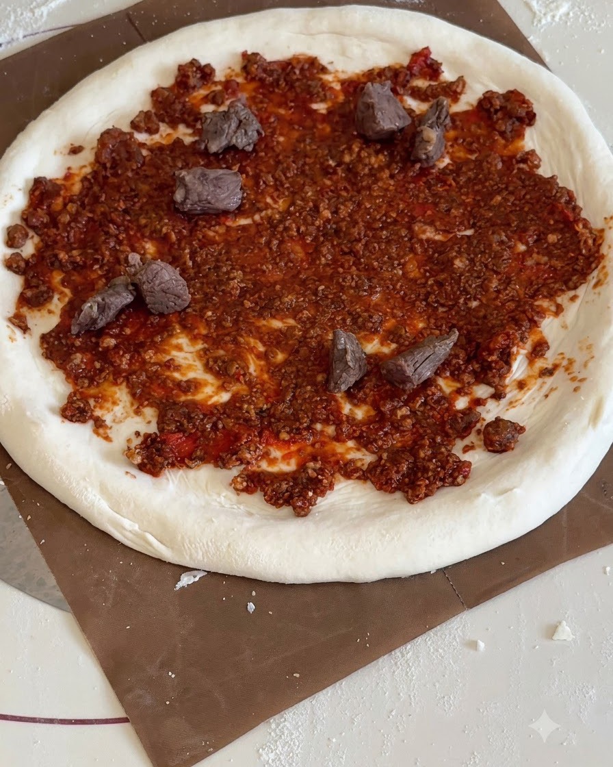Trójkątne kawałki żółtego ananasa i mięsa wołowego rozłożone na pizzy posmarowanej czerwonym sosem.