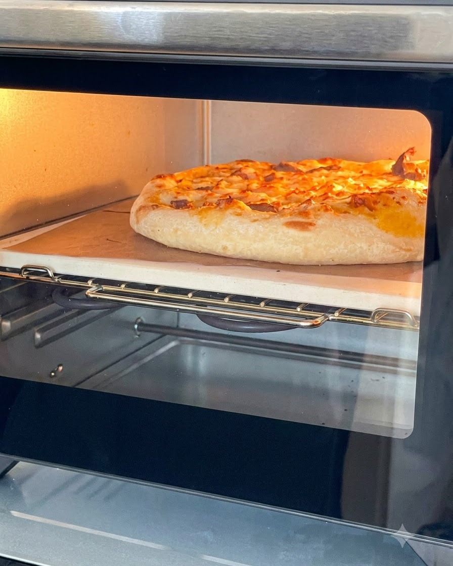 Złocista, upieczona pizza z roztopionym serem wewnątrz małego piecyka, na kamieniu do pieczenia.