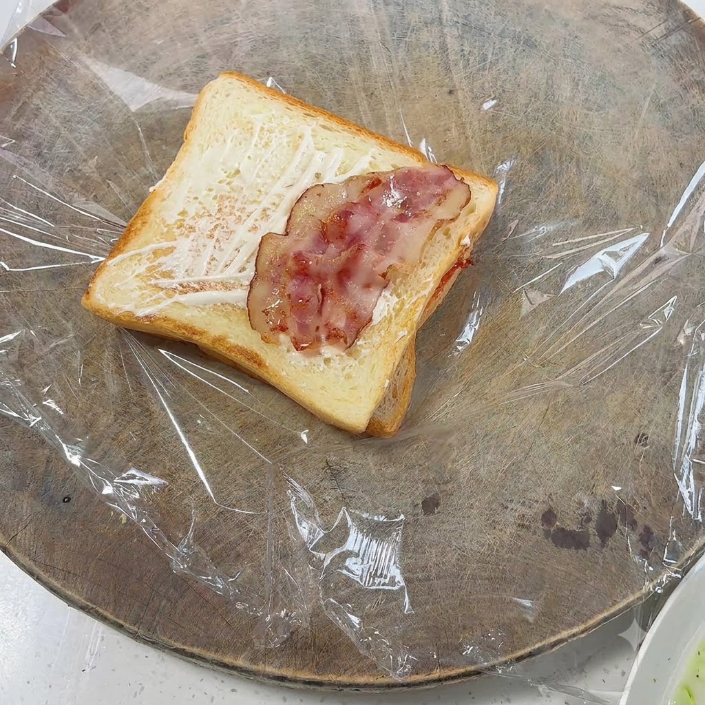Kawałki usmażonego boczku ułożone na toście posmarowanym majonezem.