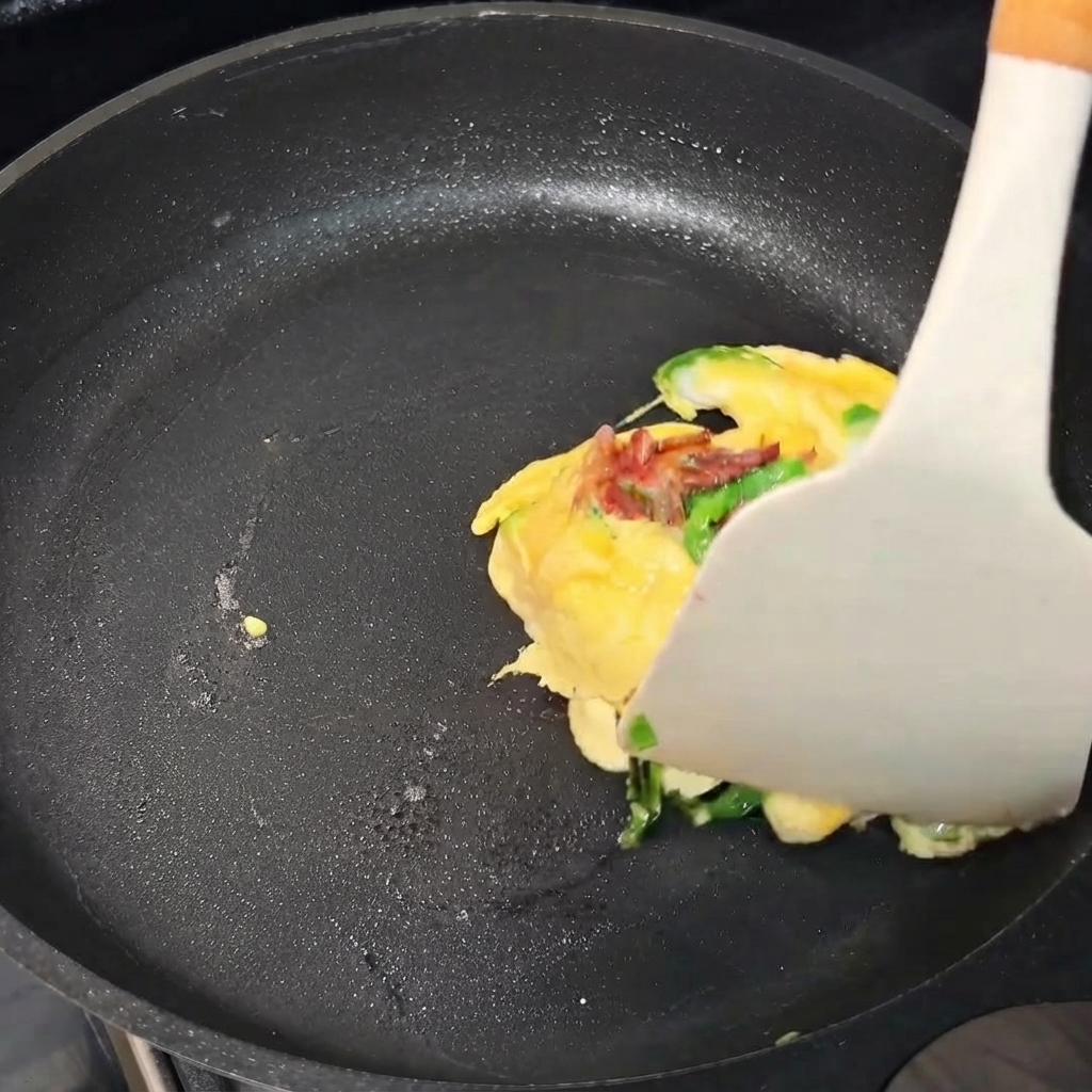 Pakiecik z omletu jajecznego składany za pomocą łopatki na patelni.