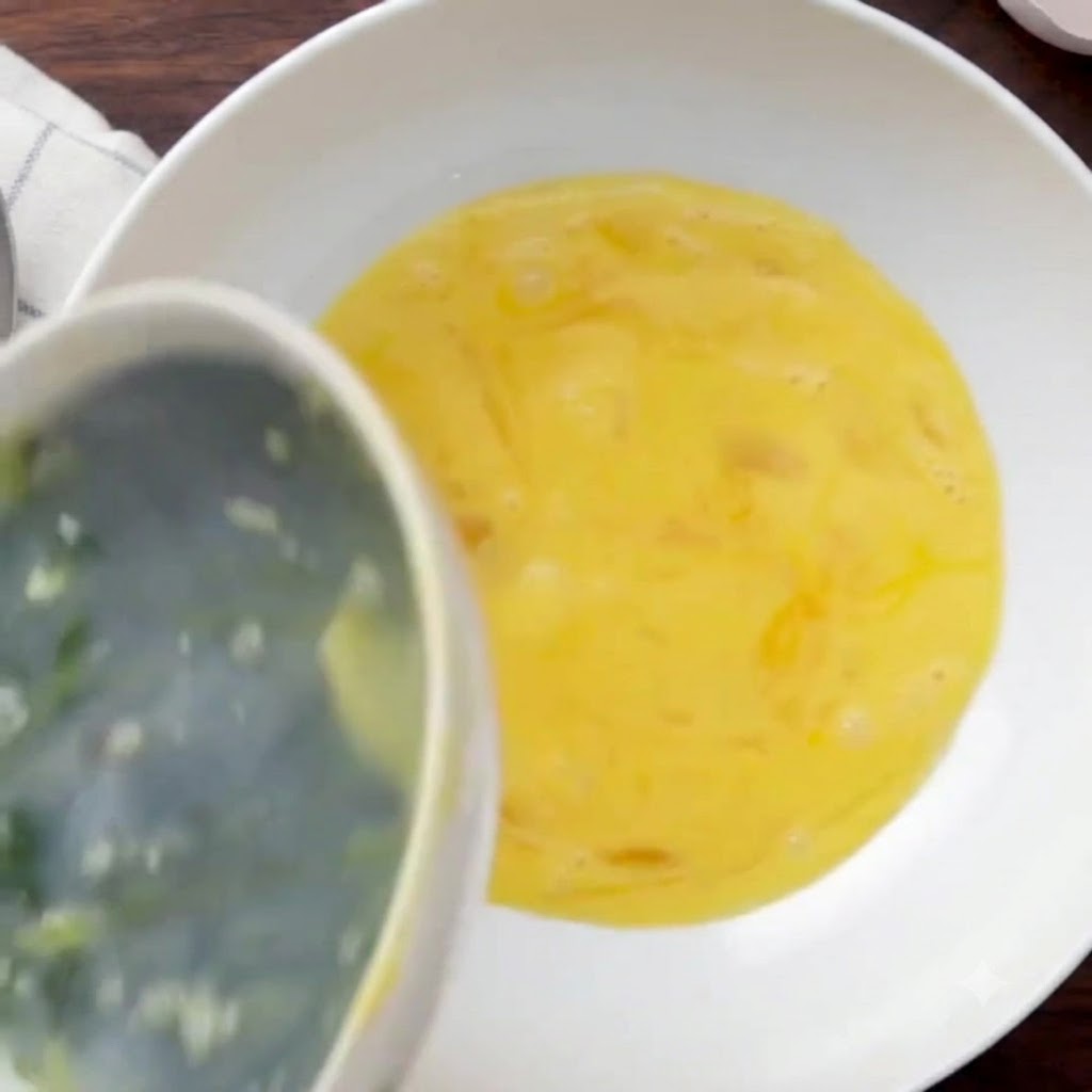 Serek wiejski wlewany do dużej białej miski wypełnionej ubitymi jajkami.