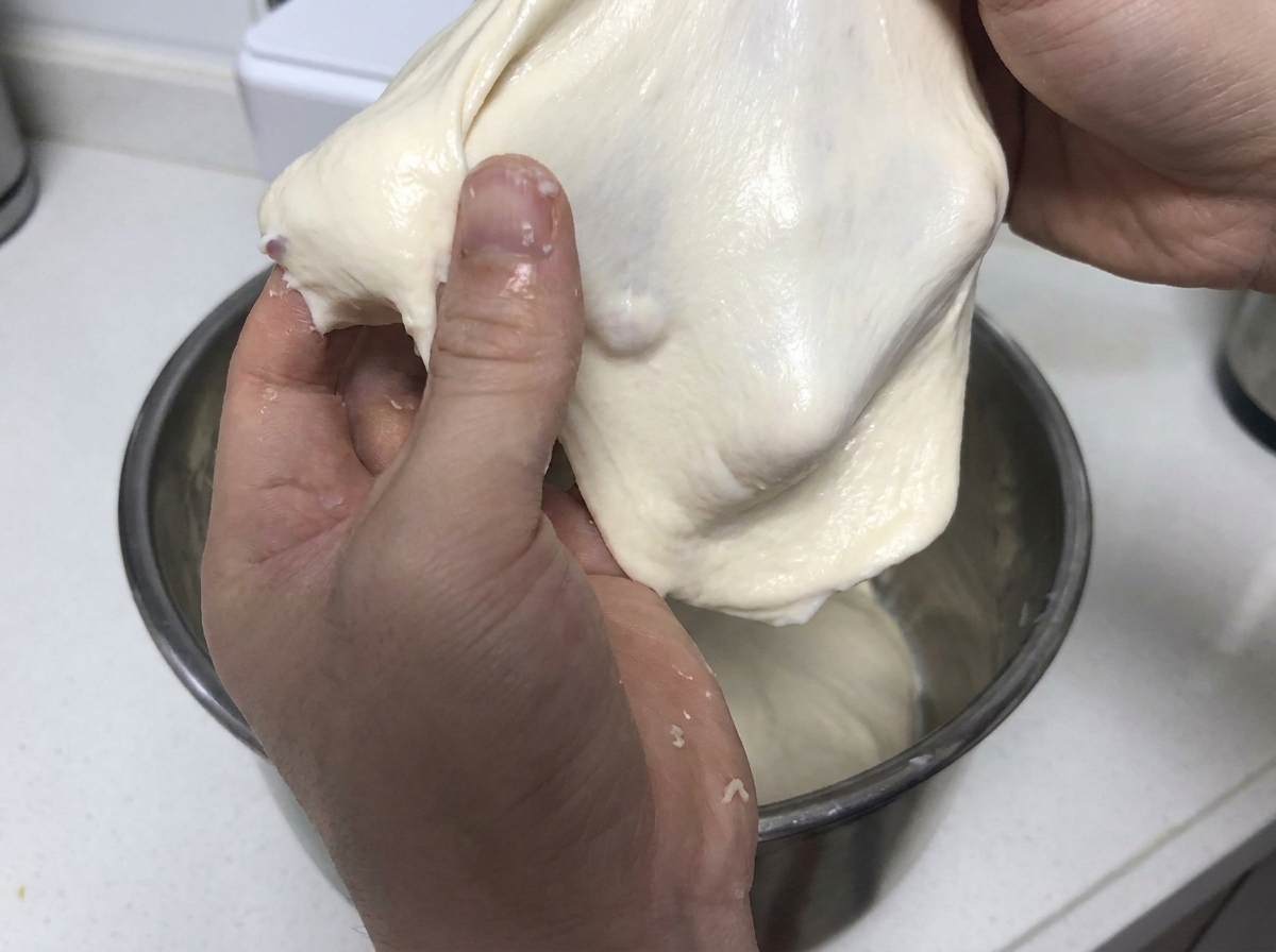 Ręce ciągnące i rozciągające miękki kawałek elastycznego białego ciasta, aby zademonstrować siłę glutenu.