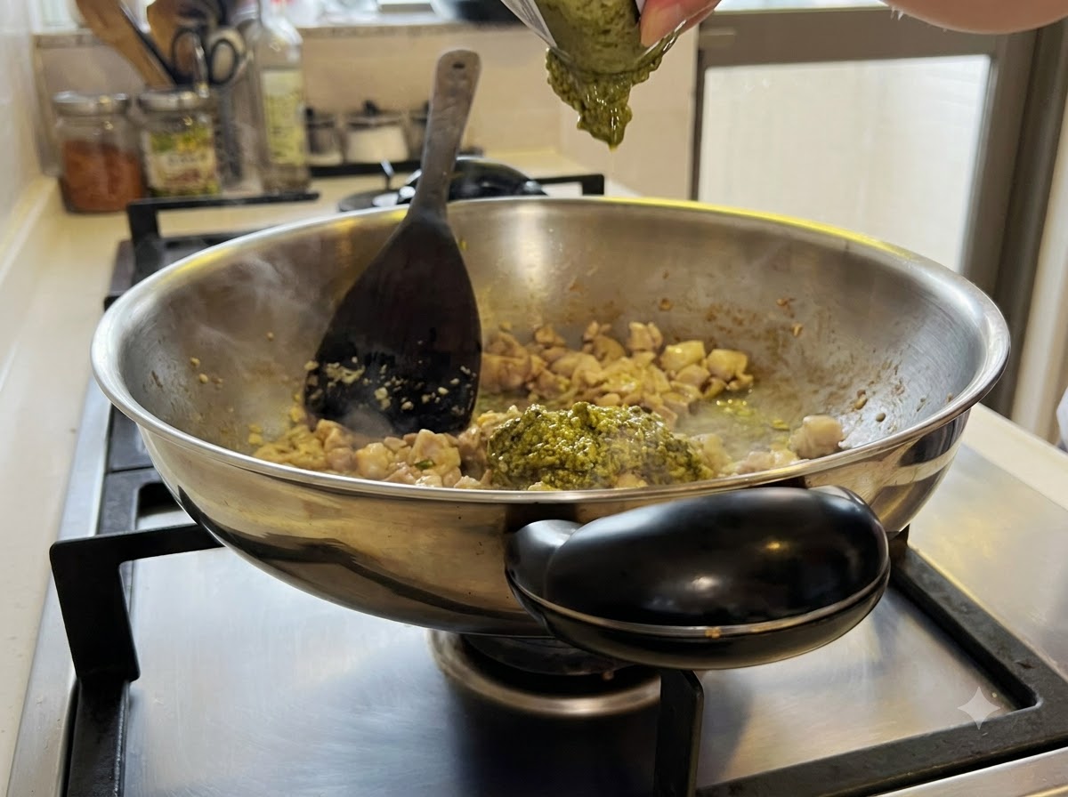 Zielony sos pesto mieszany z mieszaniną kurczaka i czosnku wewnątrz woka.