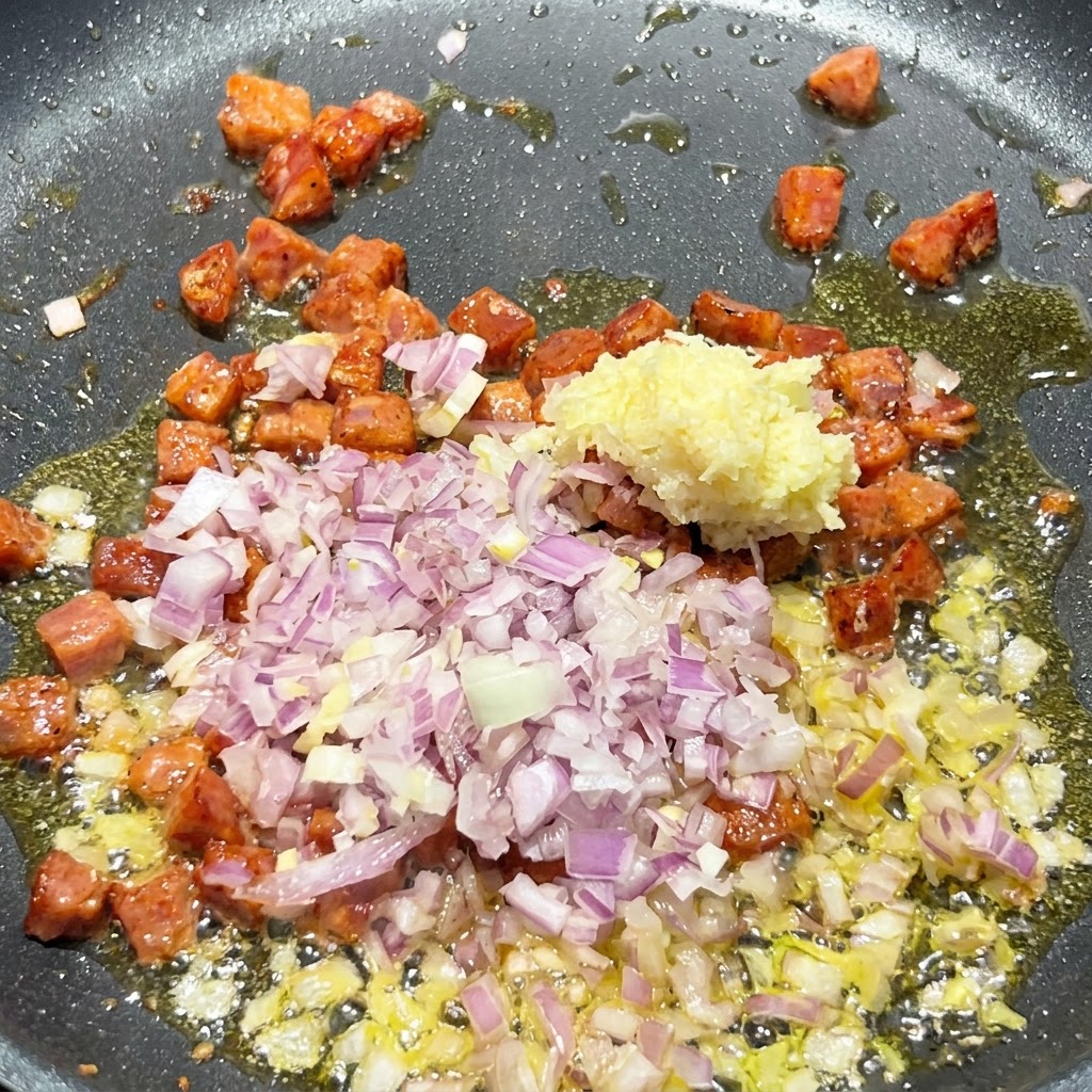 Pokrojona w kostkę czerwona cebula i posiekany czosnek dodawane do skwierczącej patelni zawierającej przyrumienione kawałki chorizo.