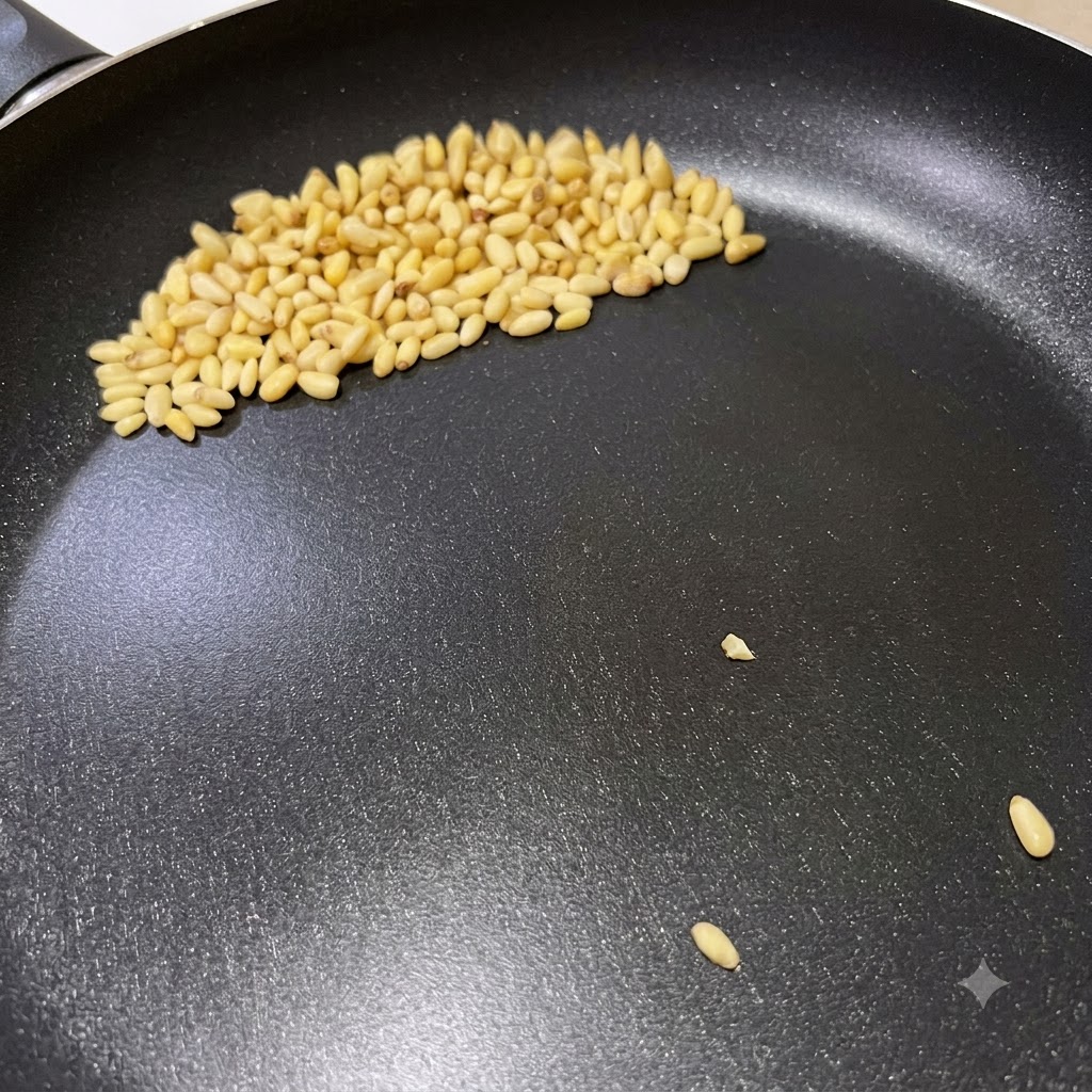 Orzechy piniowe brązowiejące na suchej patelni podczas przygotowywania włoskiego makaronu z pesto.