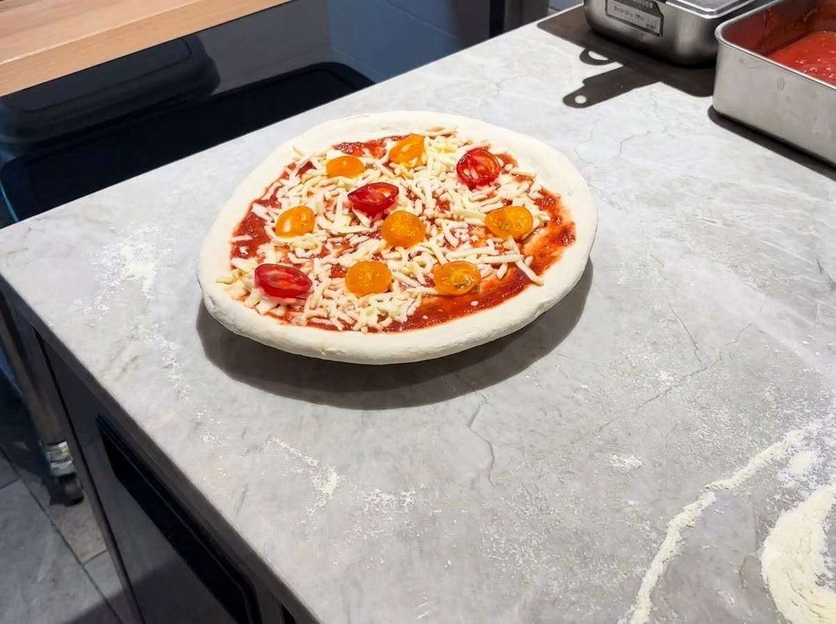 W pełni zmontowana pizza spoczywająca na metalowej łopacie na marmurowym blacie.