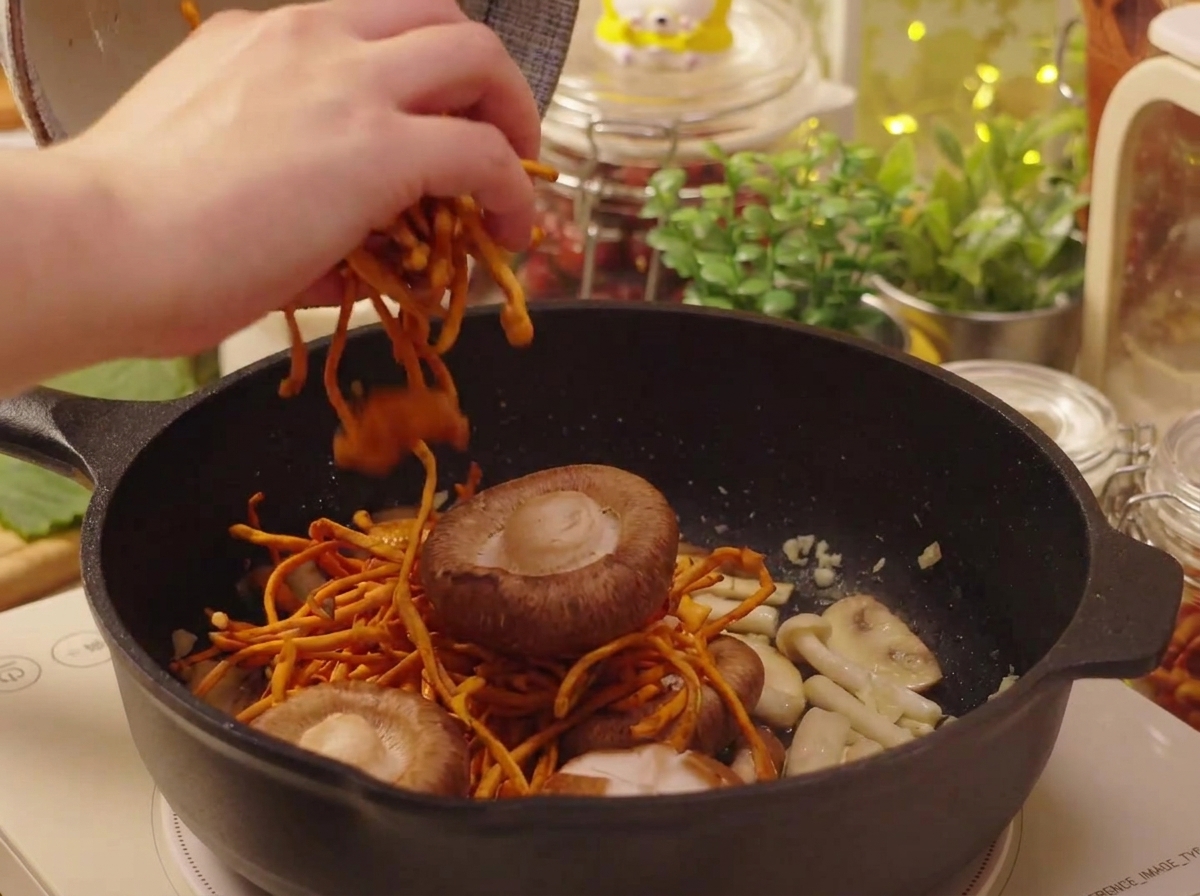Namoczone grzyby shiitake i kordyceps dodawane do patelni.