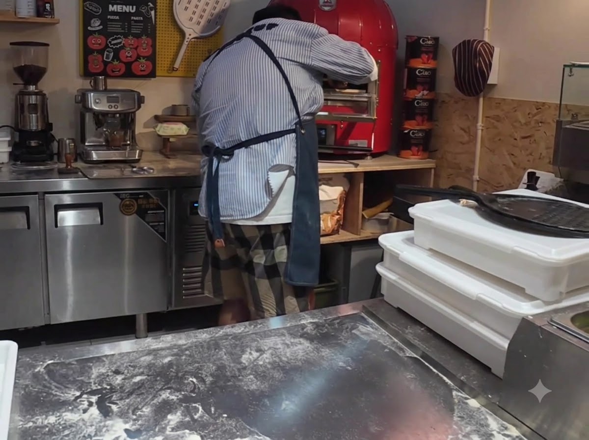 Pizza wsuwana za pomocą łopaty do jasnoczerwonego komercyjnego elektrycznego pieca do pizzy.