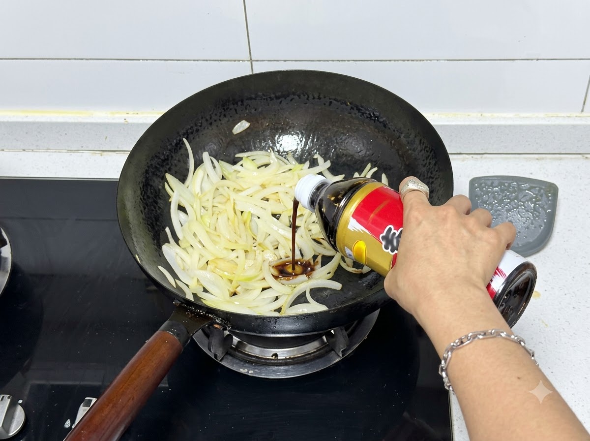 Sos sukiyaki wlewany z butelki do woka wypełnionego podsmażoną cebulą.