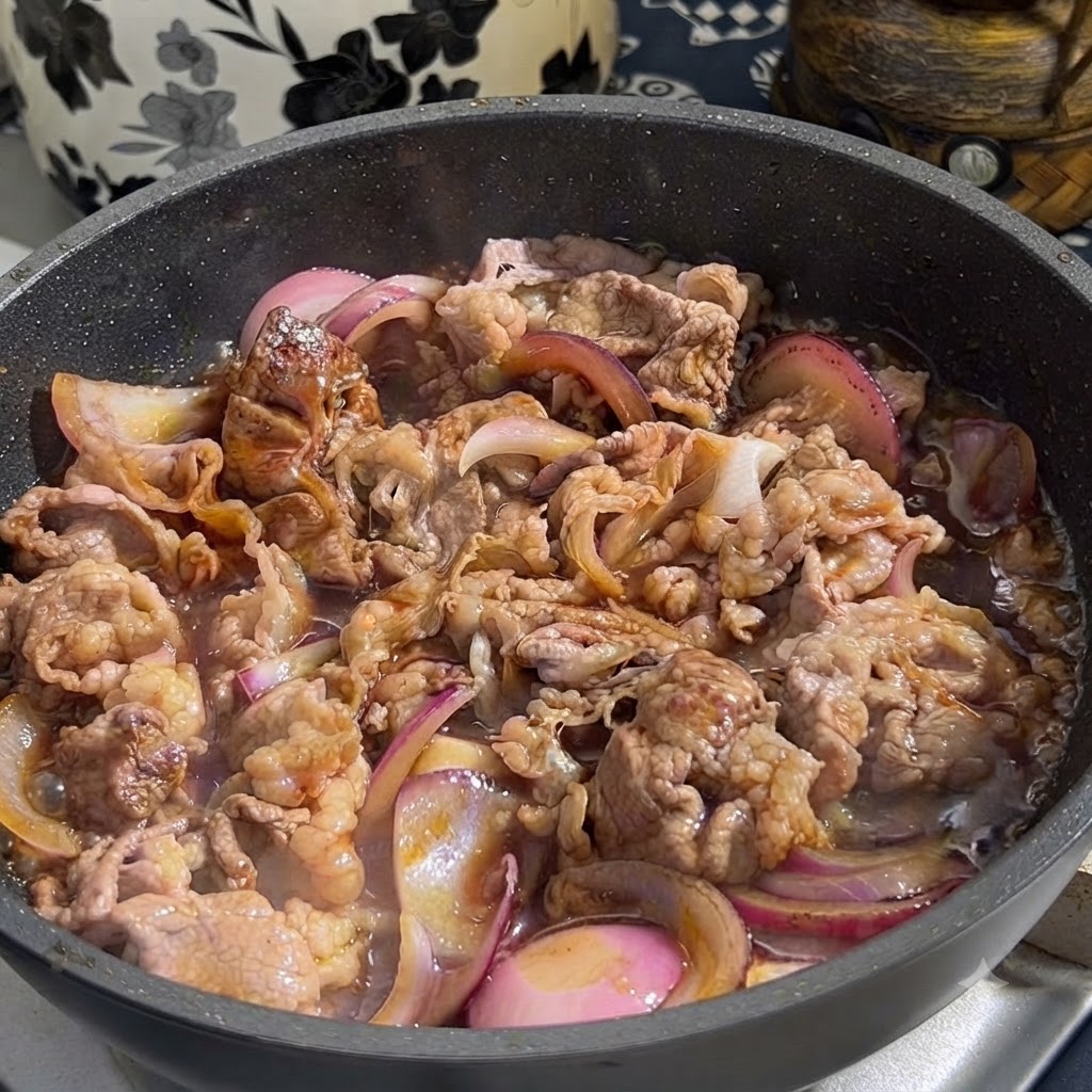 Sos teriyaki wlewany z pojemnika na patelnię zawierającą podsmażoną wołowinę i pokrojoną czerwoną cebulę.