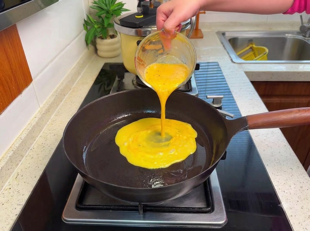Ubitą masę jajeczną wlewaną na rozgrzaną patelnię na kuchence, formującą miękkie grudki na małym ogniu.