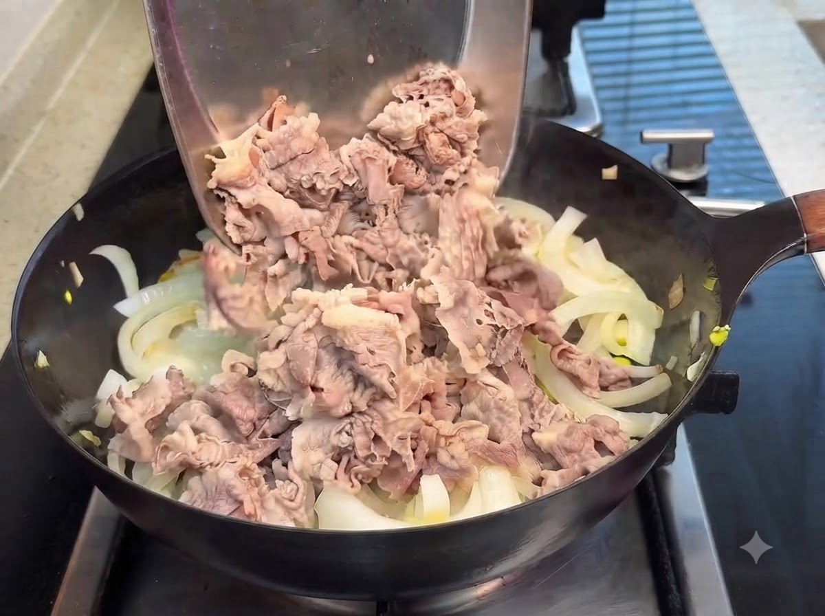 Zblanszowane plasterki wołowiny przekładane metalową łopatką na patelnię z przezroczystą cebulą, z polanym na wierzch sosem teriyaki.