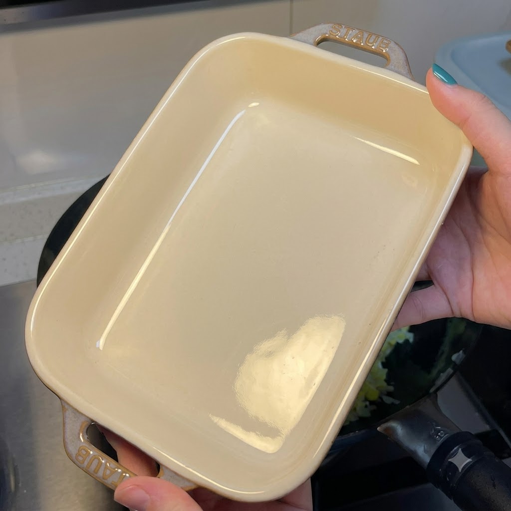 Osoba trzymająca puste prostokątne białe ceramiczne naczynie nad wokiem ze smażonym ryżem i jajkiem.