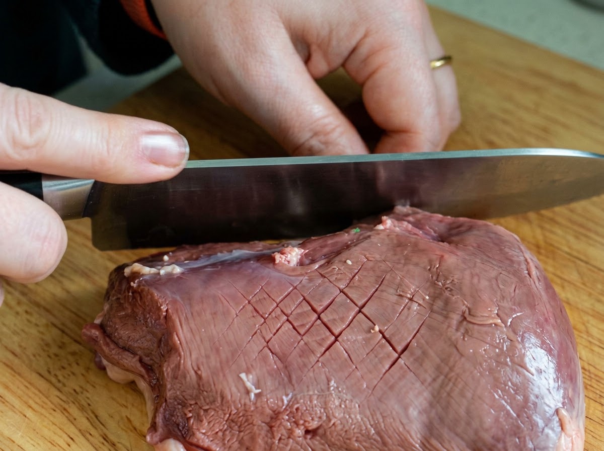 Nóż szefa kuchni nacinający wzór w kratkę na surowej skórce kaczki na drewnianej desce.