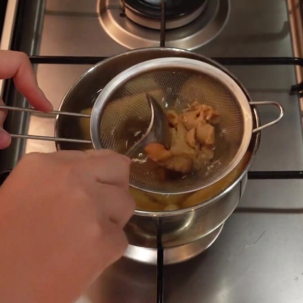 biała pasta miso mieszana w metalowym sitku zanurzonym w garnku z gorącą zupą za pomocą łyżki.