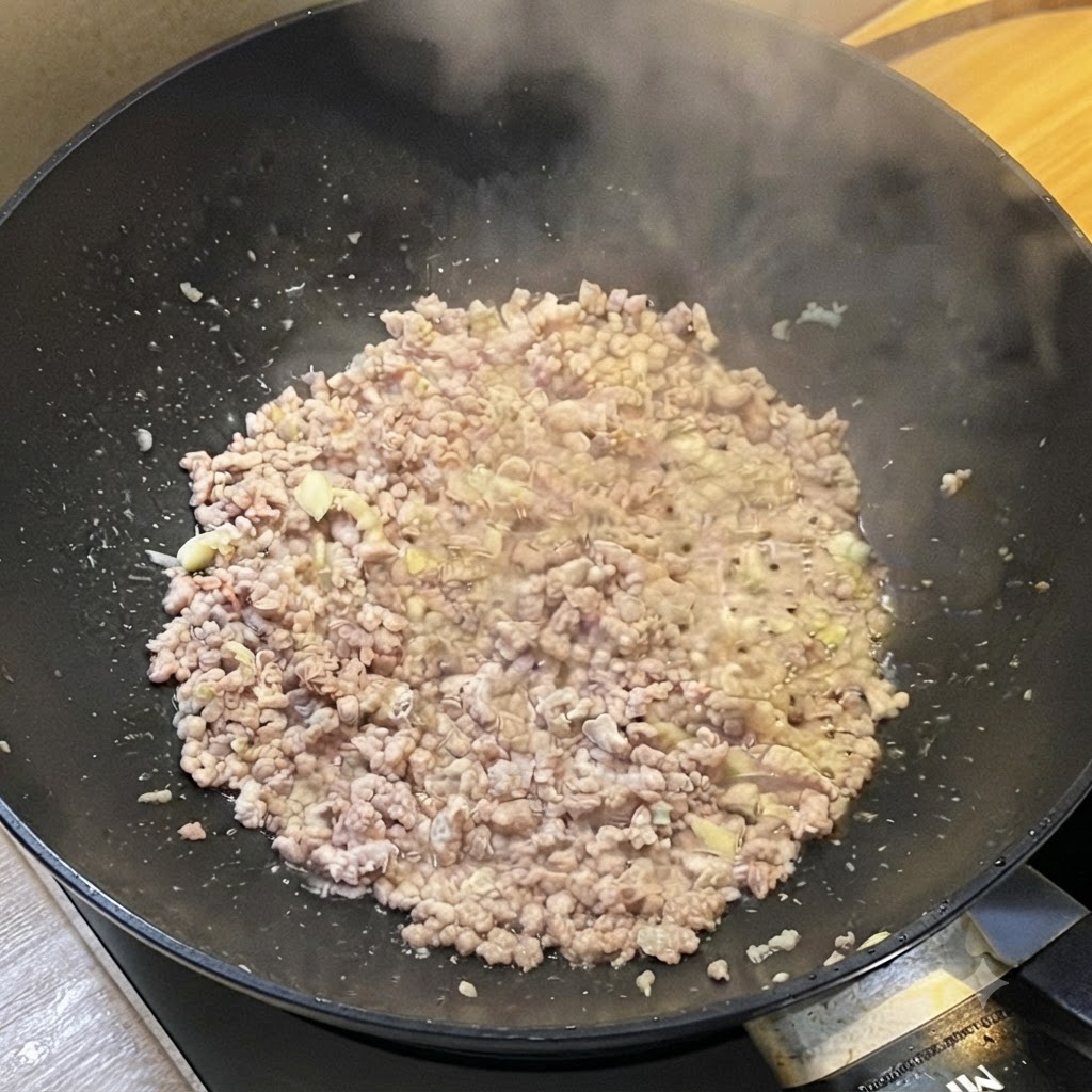 Wok wypełniony zrumienionym mielonym mięsem uwalniającym parę podczas doprawiania płynnymi sosami.