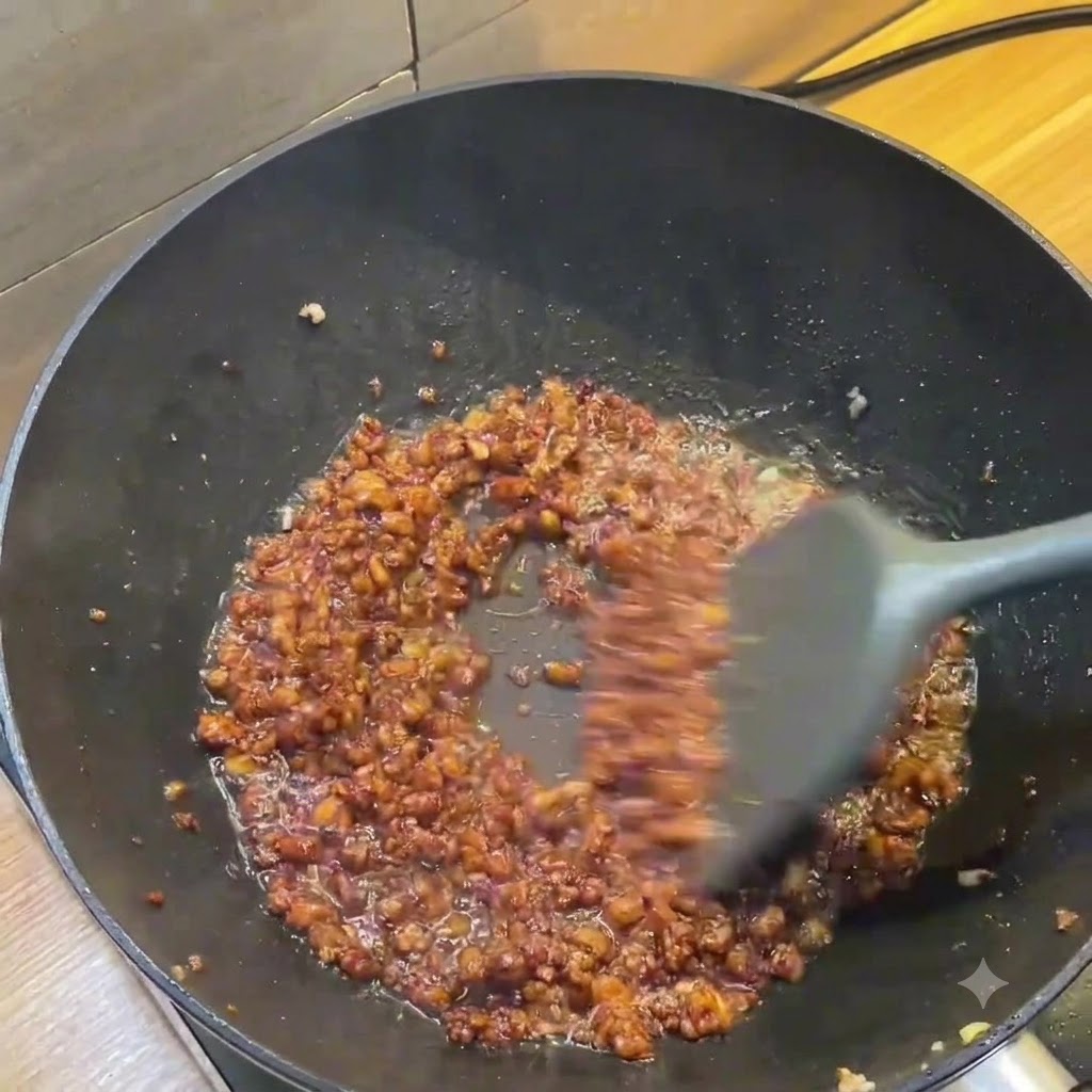 Ciemny wok pokazujący bogaty brązowy sos z mielonego mięsa mieszany szarą szpatułką.