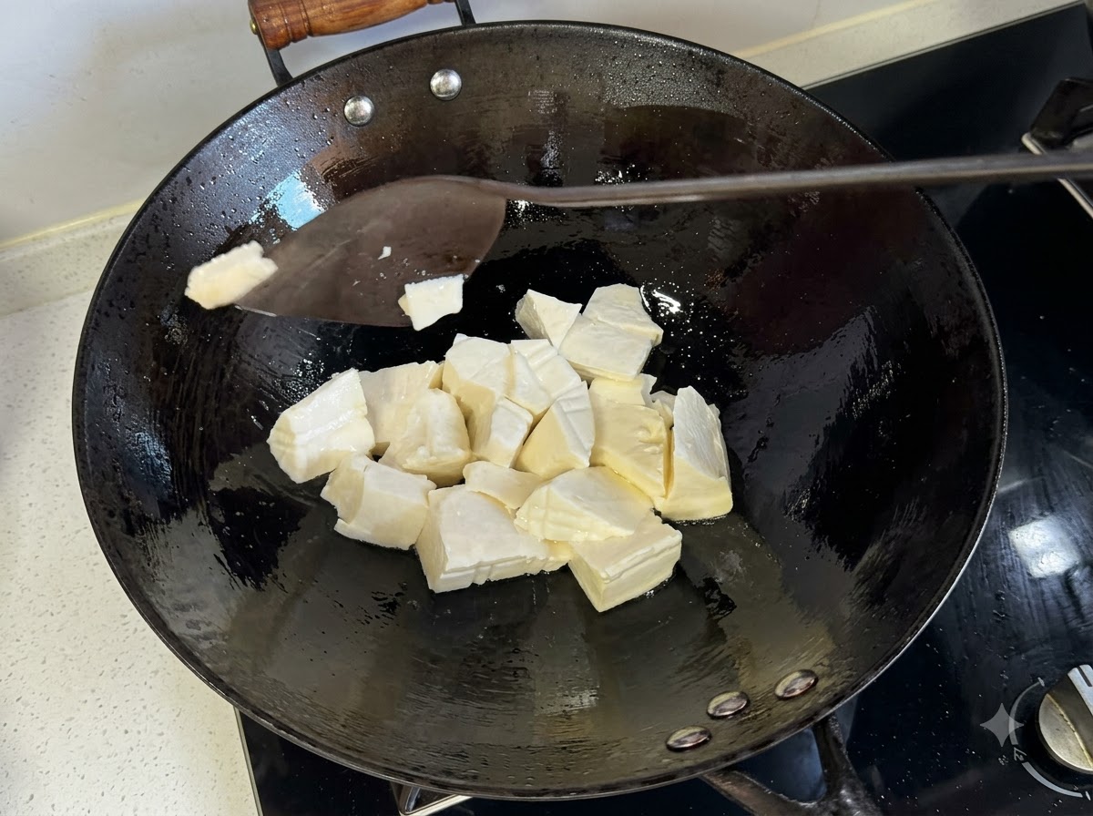 Łopatka krojąca miękkie tofu na kawałki wewnątrz gorącego woka.