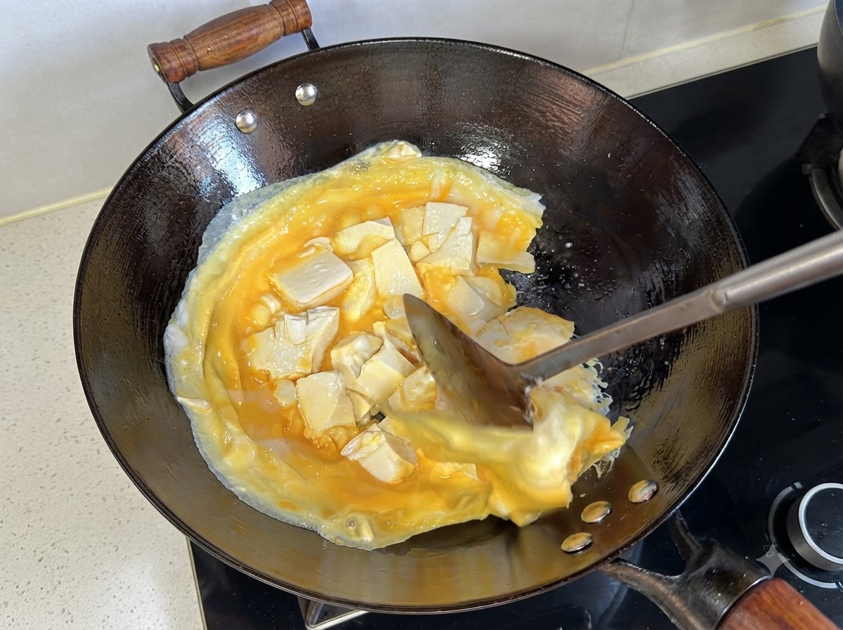 Łopatka podnosząca i odwracająca ściętą warstwę jajek i tofu w woku.