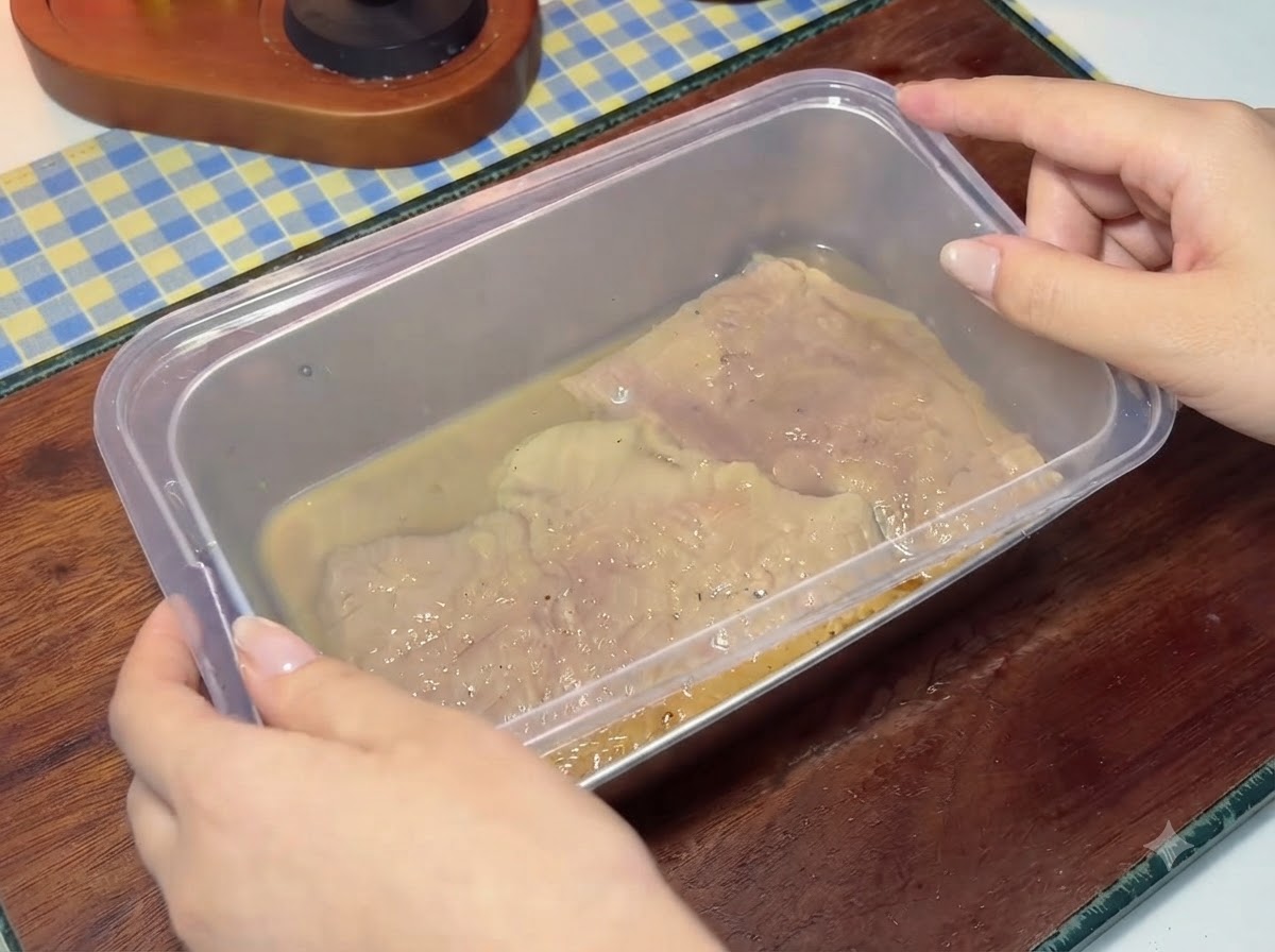 Plastikowa pokrywka nakładana na pojemnik wypełniony zamarynowanymi kotletami wieprzowymi i płynem.