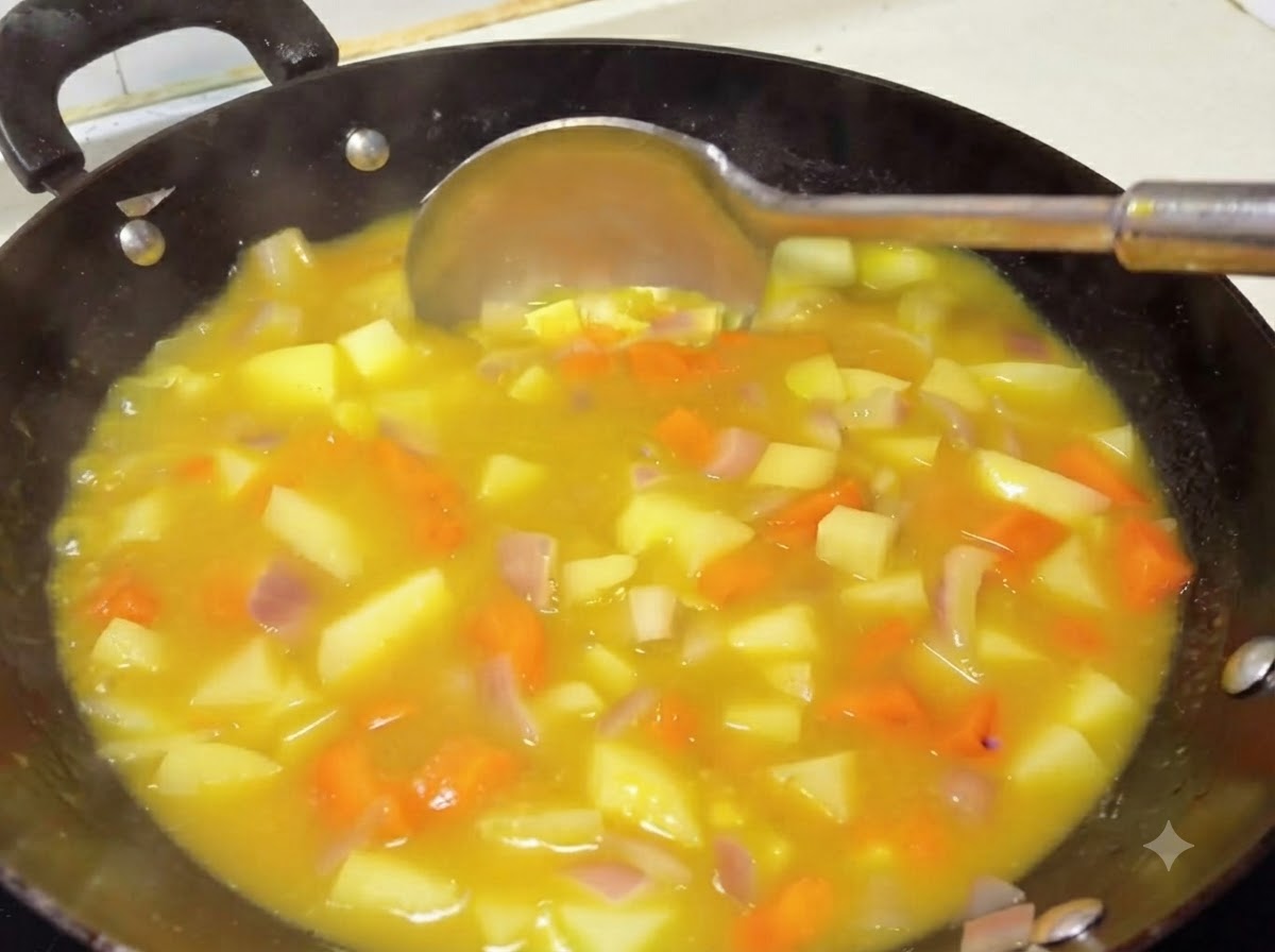Chochla mieszająca gęsty, bogaty żółty sos curry z ziemniakami i marchewką w woku.